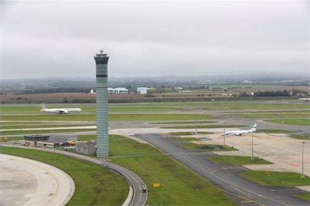 Aéroport de Paris-Charles-de-Gaulle : tour de contrôle Nord et aire de stationnement avec en arrière-plan, un Boeing B 777 d'Air France au décollage 